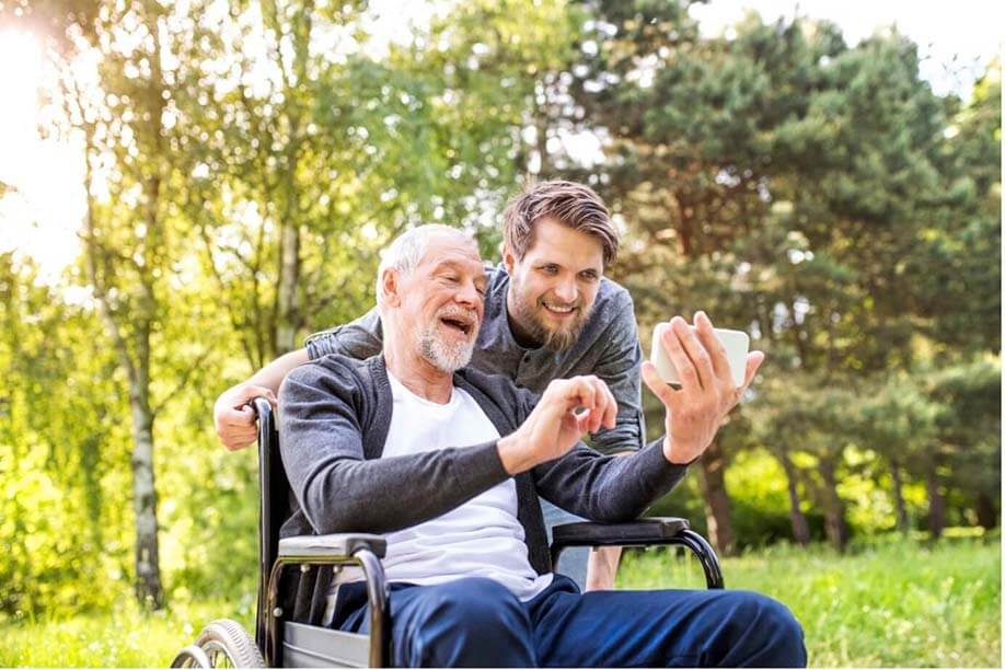 An elderly individual on his phone being supported by a young adult
