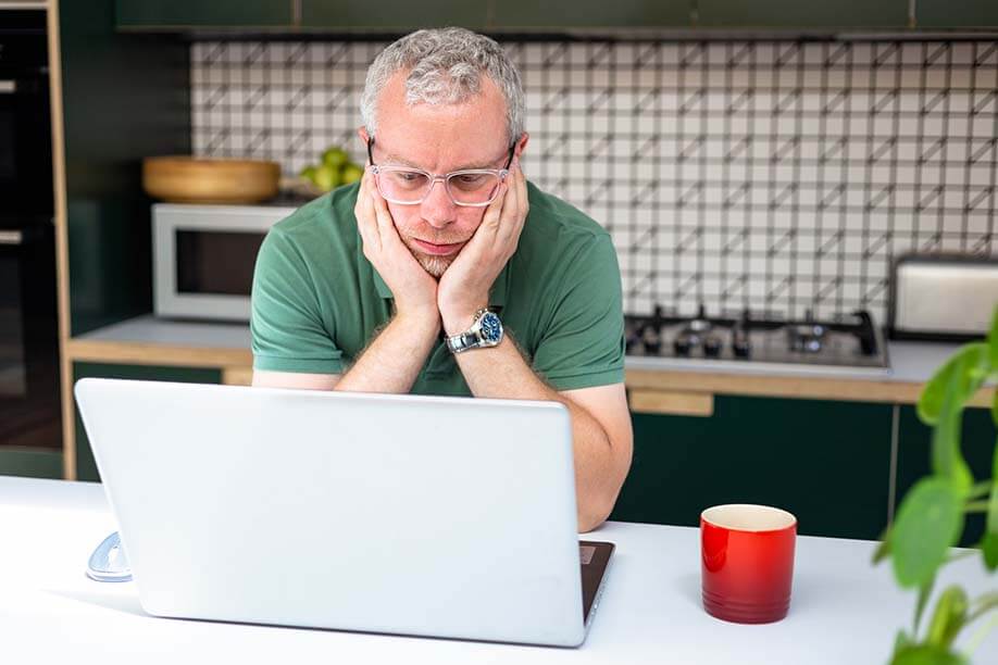 bored man looking at laptop in his kitchen